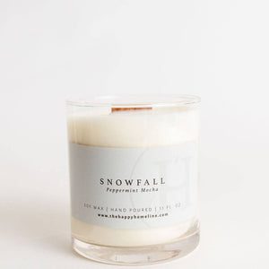 A hand-poured soy wax candle in a clear glass jar with a white paper label reading 'SNOWFALL Peppermint Meika' and a small copper-colored wick, set against a seamless white background.