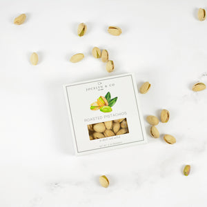 Box of roasted pistachios on a white surface with scattered pistachios around
