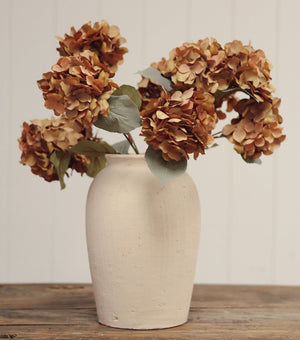 Beige ceramic vase with dried brown flowers on a wooden surface