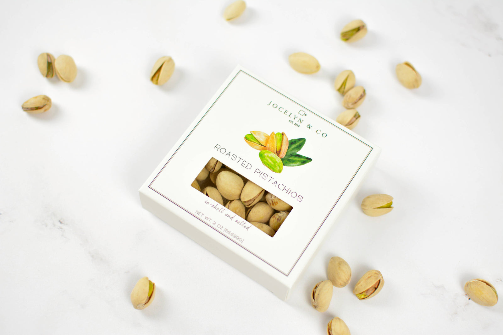 Box of roasted pistachios on a white surface with scattered pistachios around