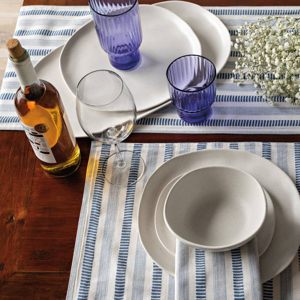 Dining table setting with plates, glasses, and cutlery on a striped tablecloth.
