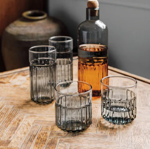 Set of smoked glass tumblers on a wooden surface with a bottle of amber liquid.