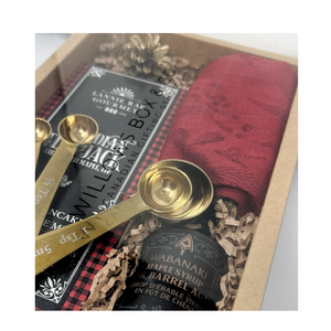Gift box with gold measuring spoons, pancake, wabanaki maple syrup, black and red packaging, and a red dishcloth.