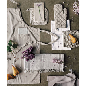 Set of kitchen accessories including an apron, oven mitts, potholders, and placemats on a textured surface with flowers and pears.