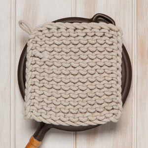 Knitted pot holder on a cast iron skillet against a wooden background
