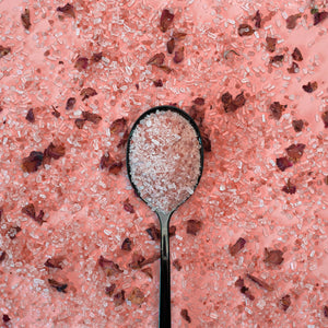 Spoon filled with pink salt on a pink salt surface