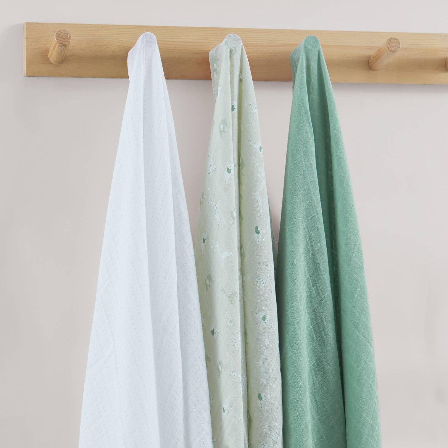Three green muslin swaddles in a white packaging with the brand 'Piccolo Bambino' visible.