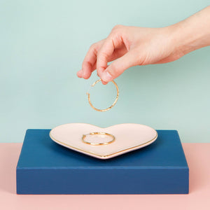 Heart-shaped jewelry dish with gold rings on a blue and pink background