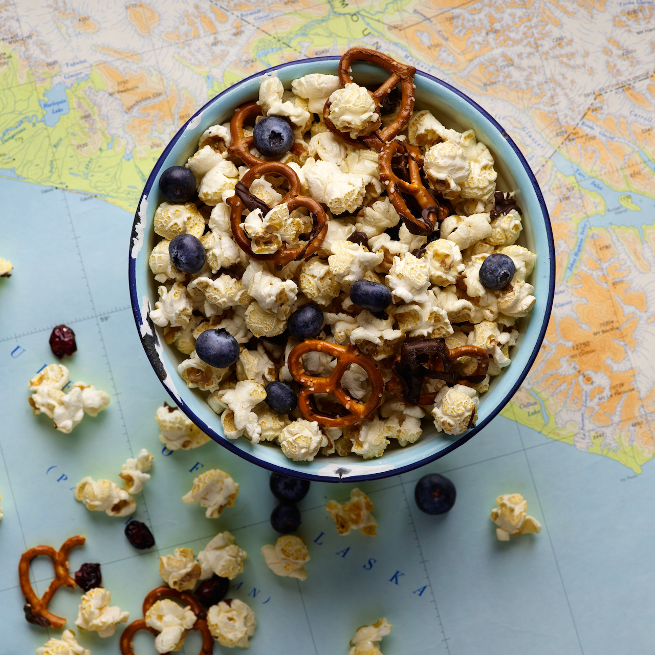 Bowl of popcorn with pretzels and blueberries on a map background