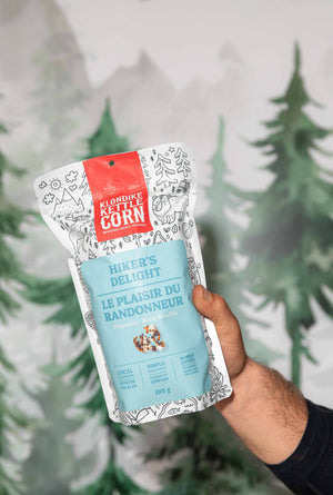 Hand holding a package of 'Hiker's Delight' against a blurred green forest background