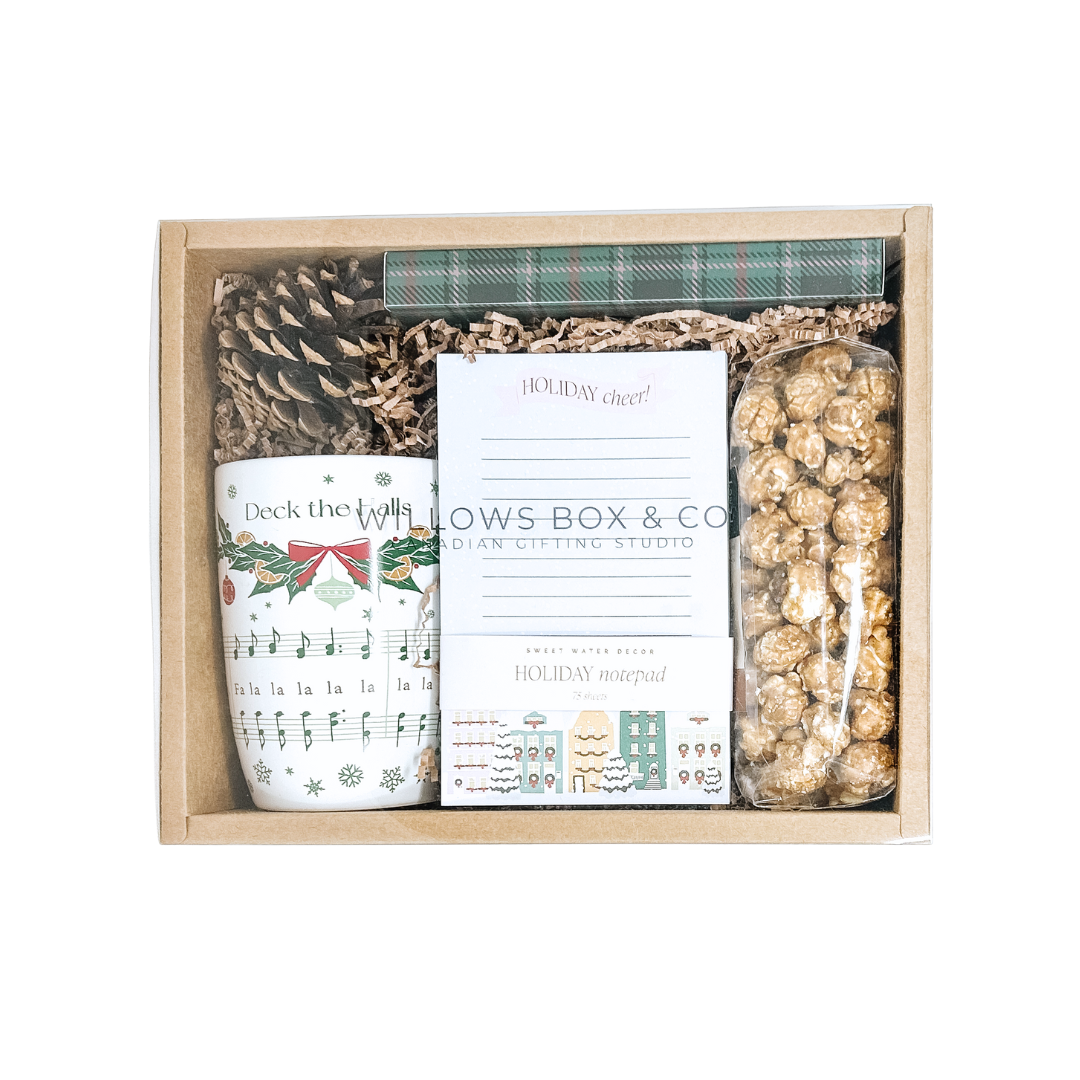Gift set with holiday mug, holiday pen set, holiday note pad, pine cone, and caramel and chocolate popcorn in a kraft box, featuring 'Willows Box & Co.' branding.