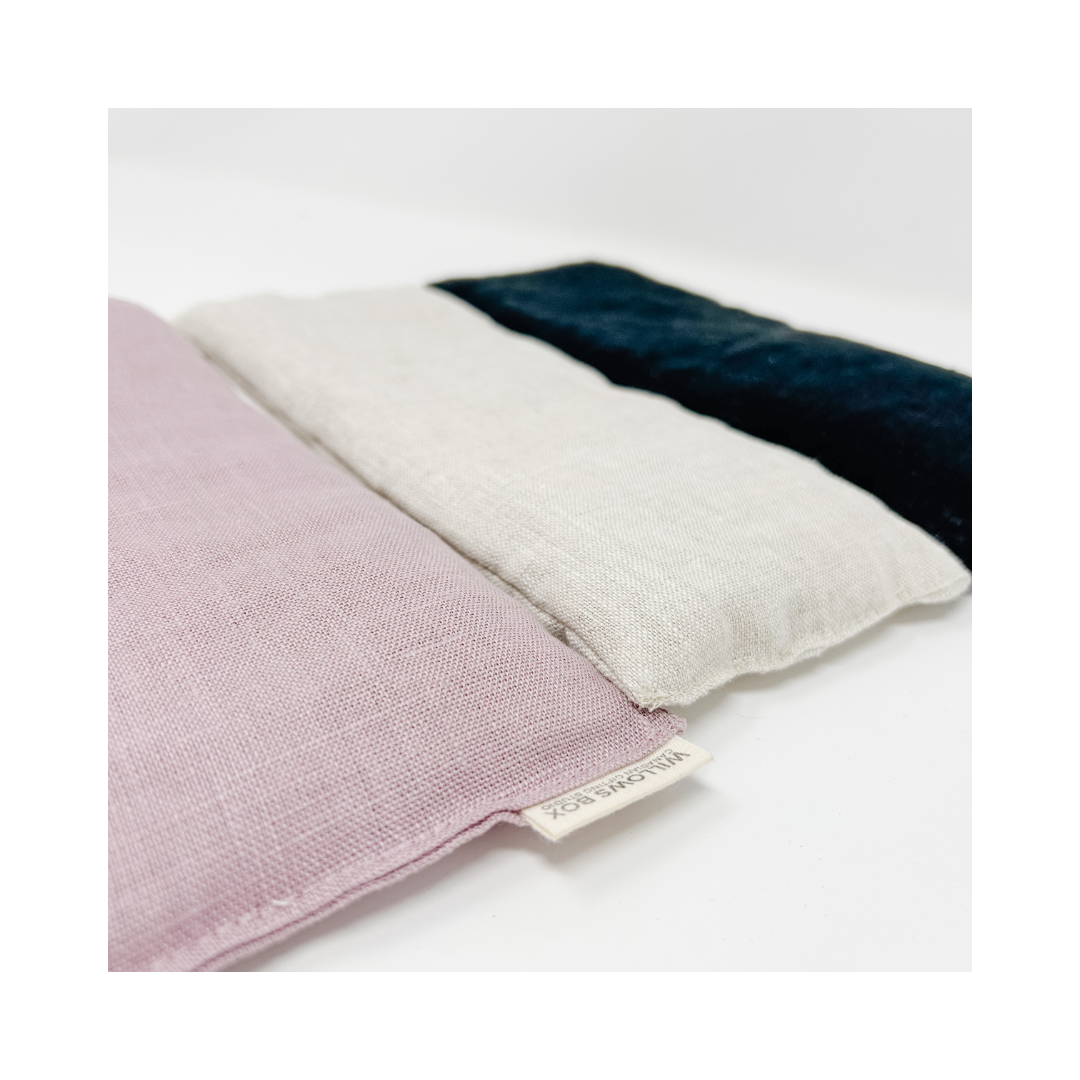 Three linen hot/cold therapy bags in pink, white, and black colors, stacked on top of each other.