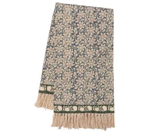 A rectangular woven throw blanket featuring an all-over floral pattern in beige and muted blue-gray, finished with a decorative border and cream fringe tassels.