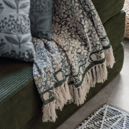 A rectangular woven throw blanket featuring an all-over floral pattern in beige and muted blue-gray, finished with a decorative border and cream fringe tassels.