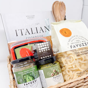 Basket with Italian food items including Favuzzi pasta and a cookbook on a white background