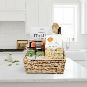 Gift basket with pasta, sauces, and a cookbook on a white background