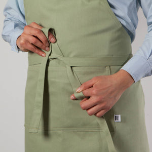 Person wearing a green apron with a visible brand label on a plain background