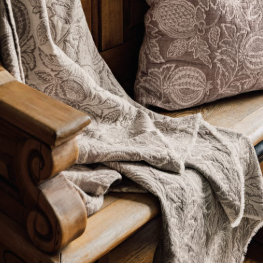A rectangular fabric napkin or tea towel with a woven botanical pattern of pomegranates and leaves in a warm taupe-brown and cream colorway, shown against a plain white background.