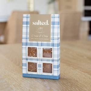 A package of 'salted.' brand Crisp & Crusty Apple + Pecan Butter Caramels standing upright on a light wood tabletop.