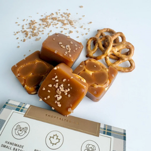 Four square pieces of caramel candy with coarse salt sprinkles, arranged with pretzels and a branded box on a white background. The box reads Shop Salted Co.