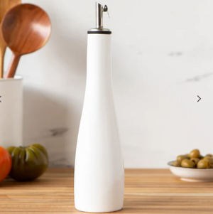 White ceramic oil bottle on a wooden surface with kitchen items in the background
