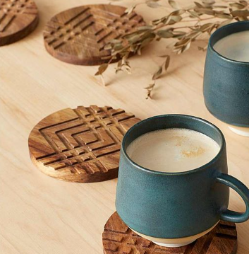Two blue mugs with wooden coasters on a light wood surface.