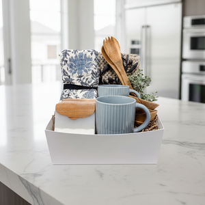 Gift basket with mugs, utensils, and a towel on a white background