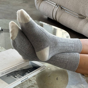 Gray socks being worn, with a glass coffee table and beige sofa in the background.